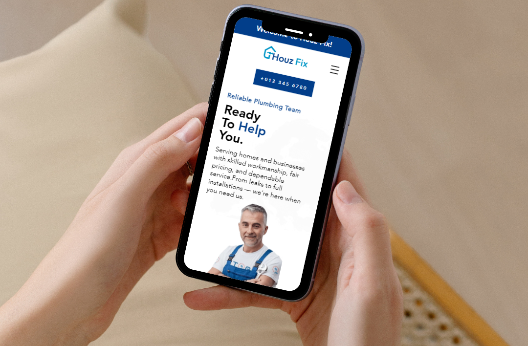 A close-up of a person holding a smartphone that displays the mobile-responsive website for 'Houz Fix' plumbing services. The screen features a clean blue and white UI with a direct call button, a professional plumber's image, and the headline 'Ready To Help You,' demonstrating an easy-to-navigate and action-oriented design for mobile users.