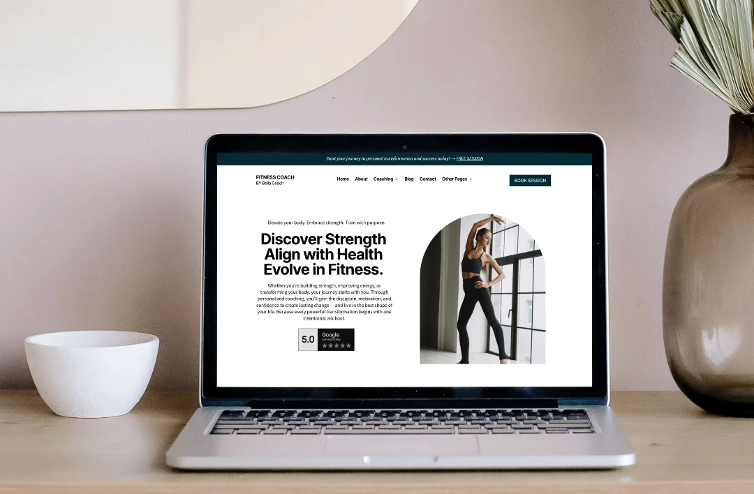 "A professional laptop mockup displaying the 'Fitness Coach' website template. The screen features a clean, modern aesthetic with a dark teal and white theme, a high-quality photo of a fitness coach in an arched frame, and the headline 'Discover Strength, Align with Health, Evolve in Fitness.' It highlights a prominent 'Book Session' call-to-action button and a 5.0 Google rating badge. The laptop is placed on a modern wooden desk in a minimalist home office setting."
