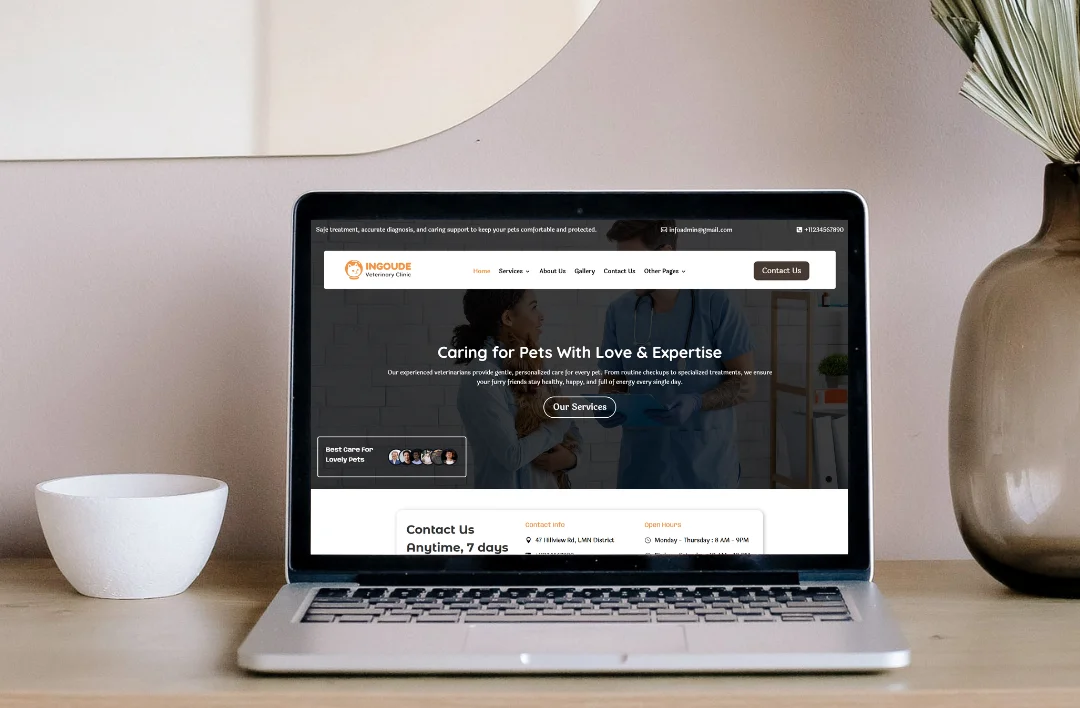 A silver laptop on a wooden desk displaying the homepage of a veterinary clinic website named "SafePaw." The screen features an orange and white theme with a main headline that reads "Caring for Pets With Love & Expertise" over a background of vets at work. Below the main image, a contact section displays the clinic's seven-day availability. The laptop is placed next to a minimalist white bowl and a brown glass vase with a dried leaf against a neutral wall.