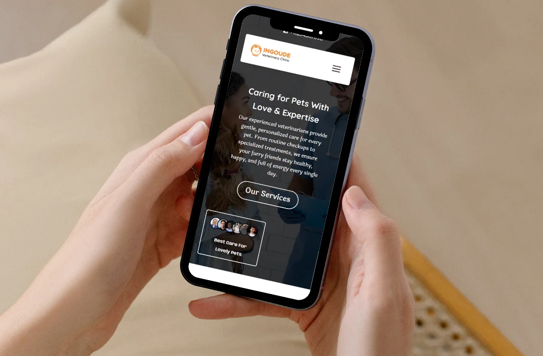 A close-up shot of a person's hands holding a smartphone that displays the mobile-responsive homepage of the "SafePaw" veterinary clinic. The screen shows a professional dark background with white and orange text featuring the headline "Caring for Pets With Love & Expertise" and a clear "Our Services" button. The layout demonstrates a clean, user-friendly mobile design for a veterinary practice.