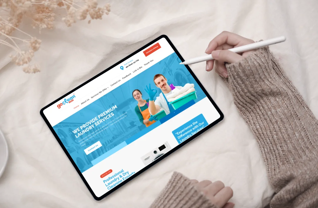 "A top-down view of a tablet and stylus on a minimalist white fabric background, displaying the 'GoClean' laundry service website template. The screen features a bright sky-blue and white theme, high-quality imagery of a professional service team, and a clear 'Schedule a Pickup' call-to-action button. The design emphasizes a neat, professional layout optimized for touch-screen navigation."