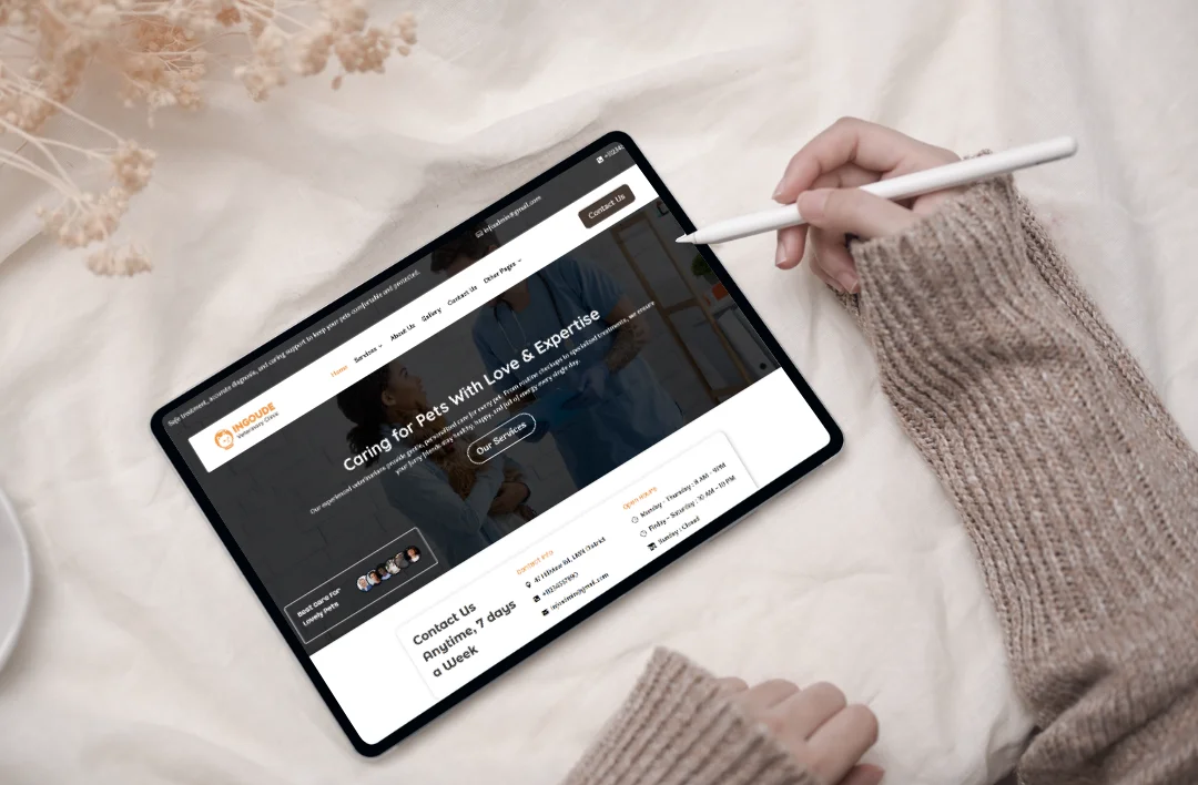 An overhead shot of a person using a stylus on a tablet that displays a veterinary clinic WordPress template. The website, branded as "SafePaw," features an orange and dark grey theme with the headline "Caring for Pets With Love & Expertise." The screen also shows a 7-day contact schedule and a call-to-action button for services. The tablet is set on a white linen background with neutral-toned dried floral accents.
