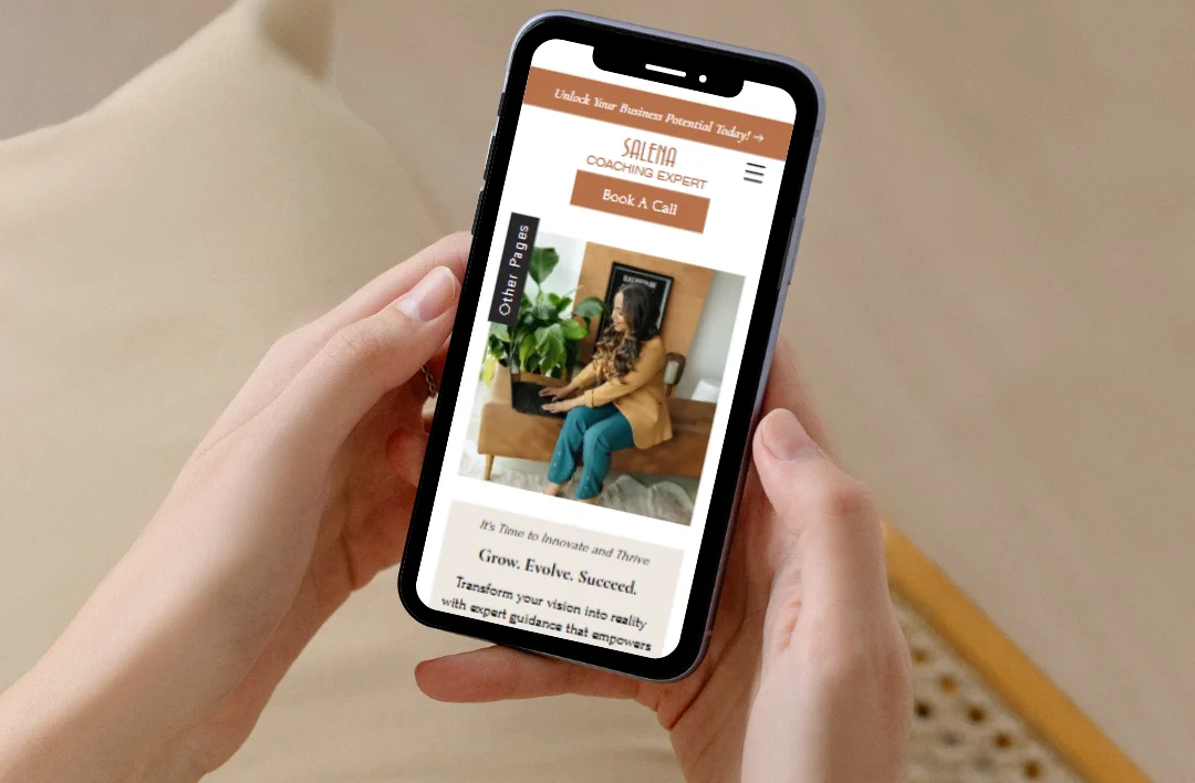 Close-up lifestyle mockup of a hand holding a smartphone displaying the 'Selena' Business Coach Wix website template. The mobile design features a warm earth-tone header, a prominent 'Book A Call' button, and a professional photo of a business woman. Styled in a bright, modern setting with minimalist aesthetics.