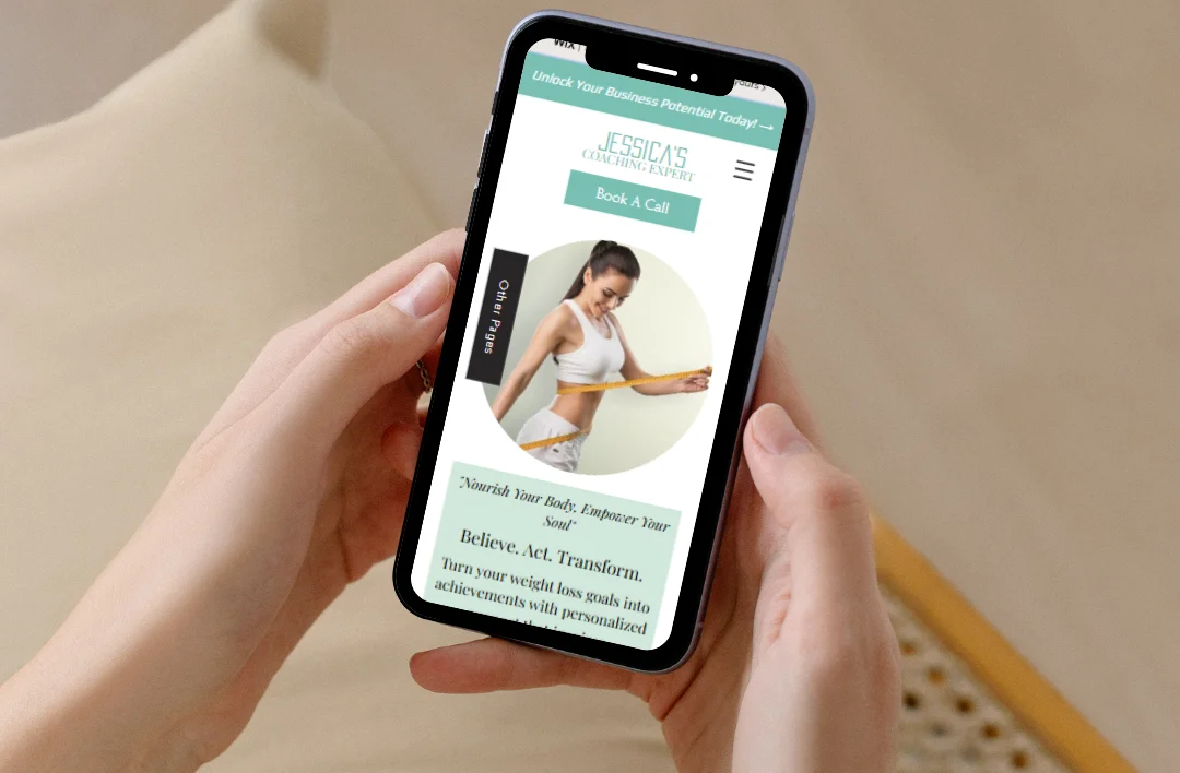 Close-up lifestyle mockup of a hand holding a smartphone displaying the 'Weight Loss Coach' website template. The mobile design features a mint green 'Book A Call' button, a professional fitness coach image, and a clean minimalist layout.