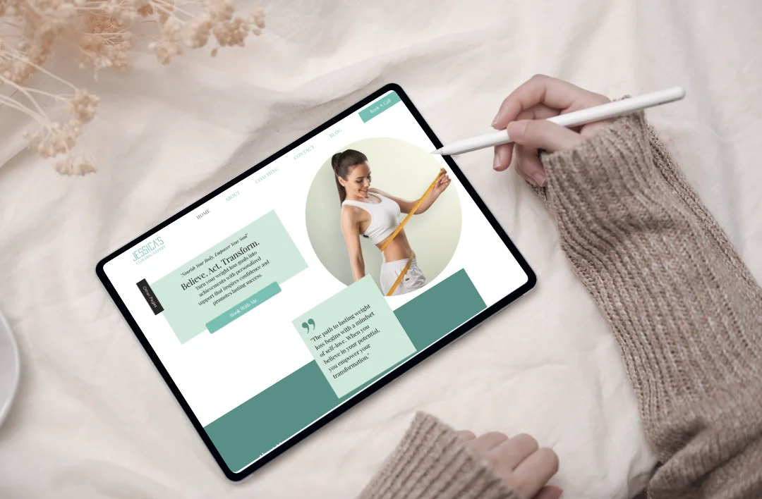 Top-down lifestyle mockup of a 'Weight Loss Coach' Wix website template displayed on a tablet with a stylus. The design features a mint green and white theme, a professional fitness coach portrait, and a clean minimalist layout. Surrounded by soft fabric and dried flowers for a high-end aesthetic.